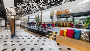A modern lobby with a geometric ceiling design, a bar area, and a seating area with colorful cushions. - Mercure Budapest Castle Hill (Budapest)