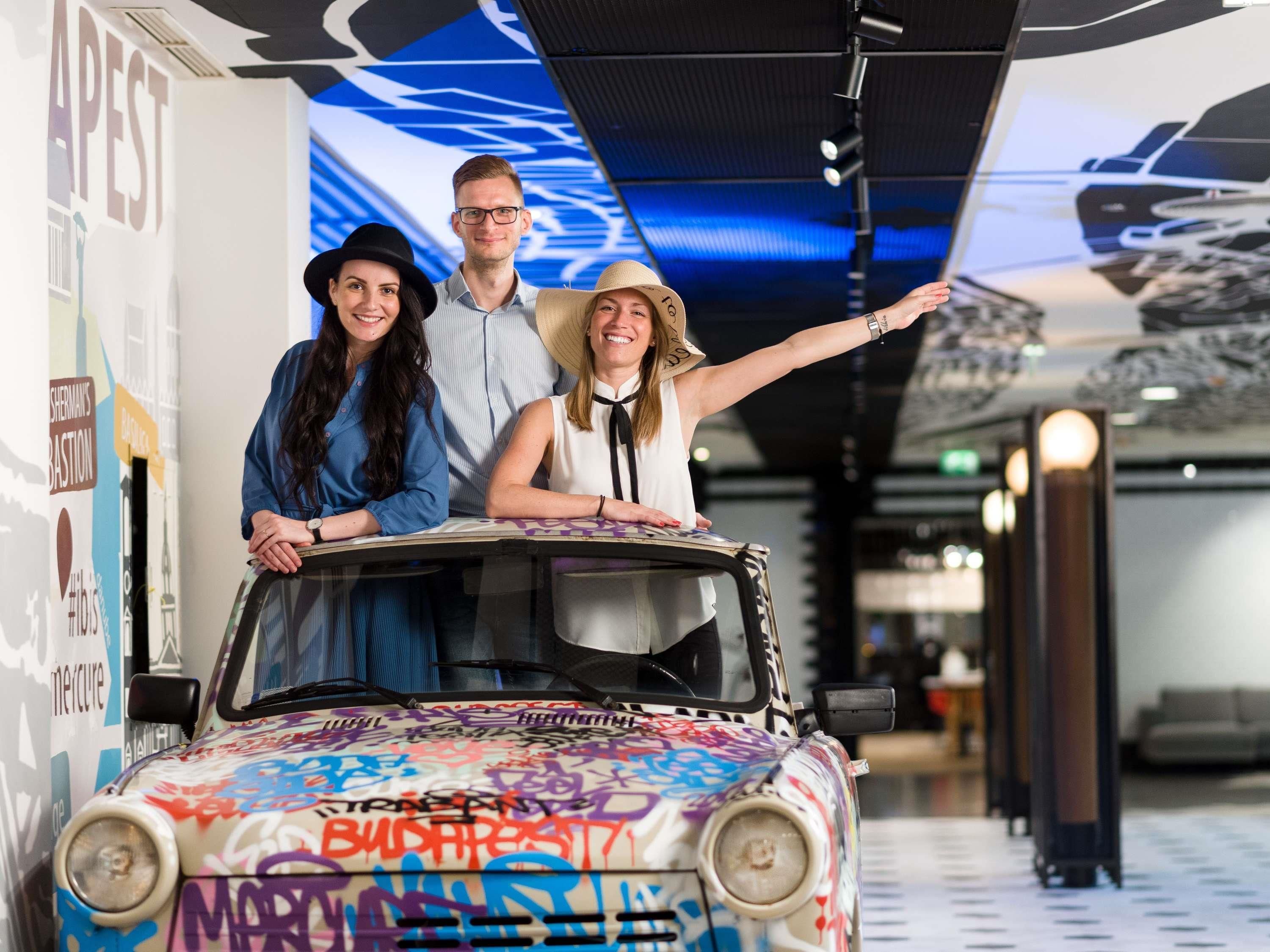 Ein Auto mit Graffiti, eine Person, die zeigt, und eine Wand mit Schrift.