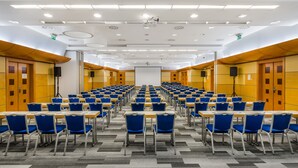 A conference room with rows of blue chairs and tables, equipped with projectors and speakers, and a large screen at the front. - Mercure Budapest Castle Hill (Budapest)