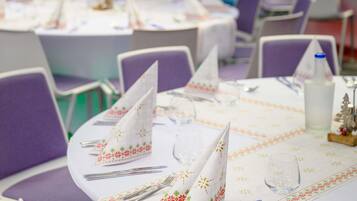 Un salón de banquetes con mesas redondas, sillas moradas y manteles blancos con motivos florales.