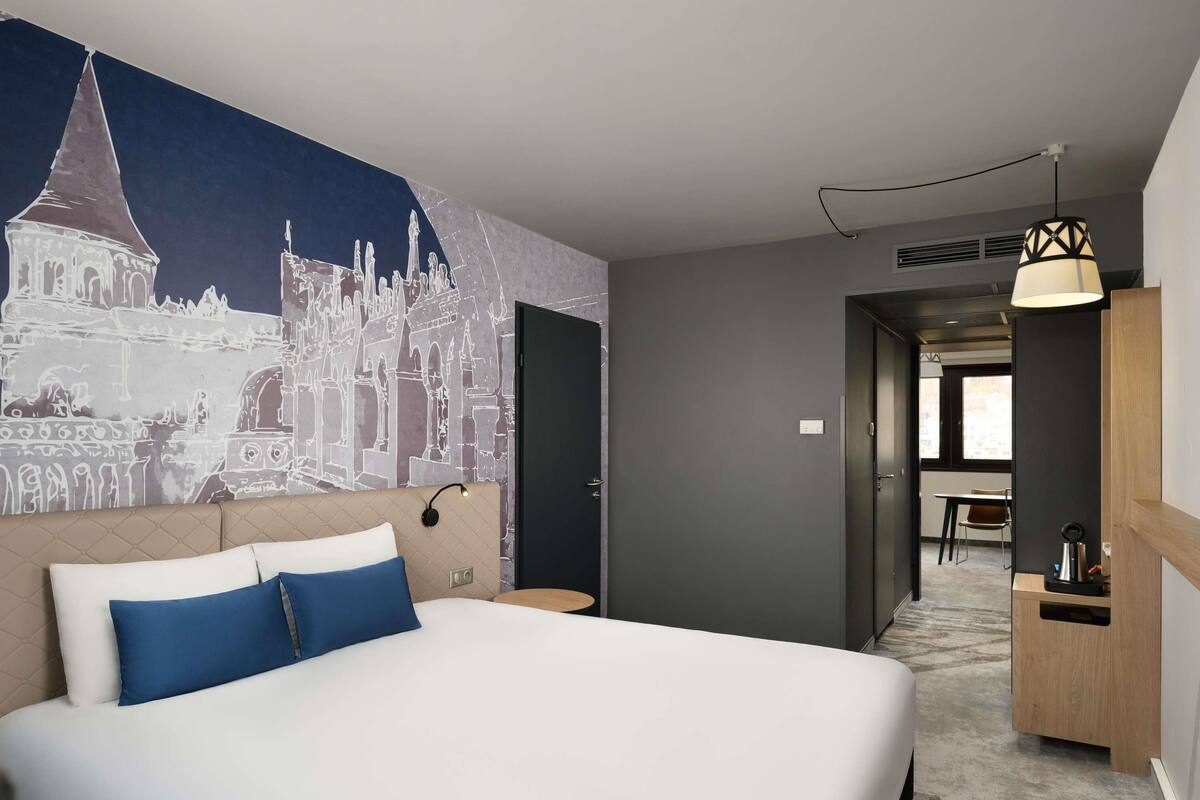 A hotel room with a large bed, a desk, a chair, and a wall mural.