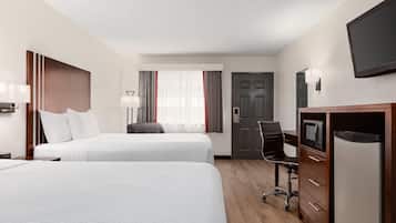 A hotel room with two beds, a desk, a chair, a TV, and a door.
