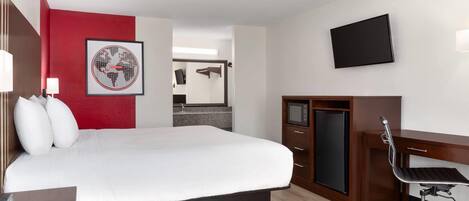A hotel room with a bed, a desk, a TV, and a red accent wall.