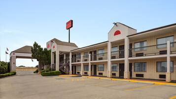 A multi-story motel with a covered entrance, a sign indicating it's a Ramada hotel, and a parking lot with marked spaces.