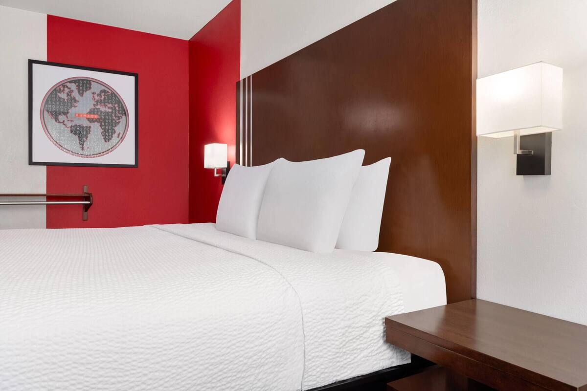 Une chambre d’hôtel comprenant un lit, une tête de lit, une lampe fixée au mur et une carte du monde encadrée.