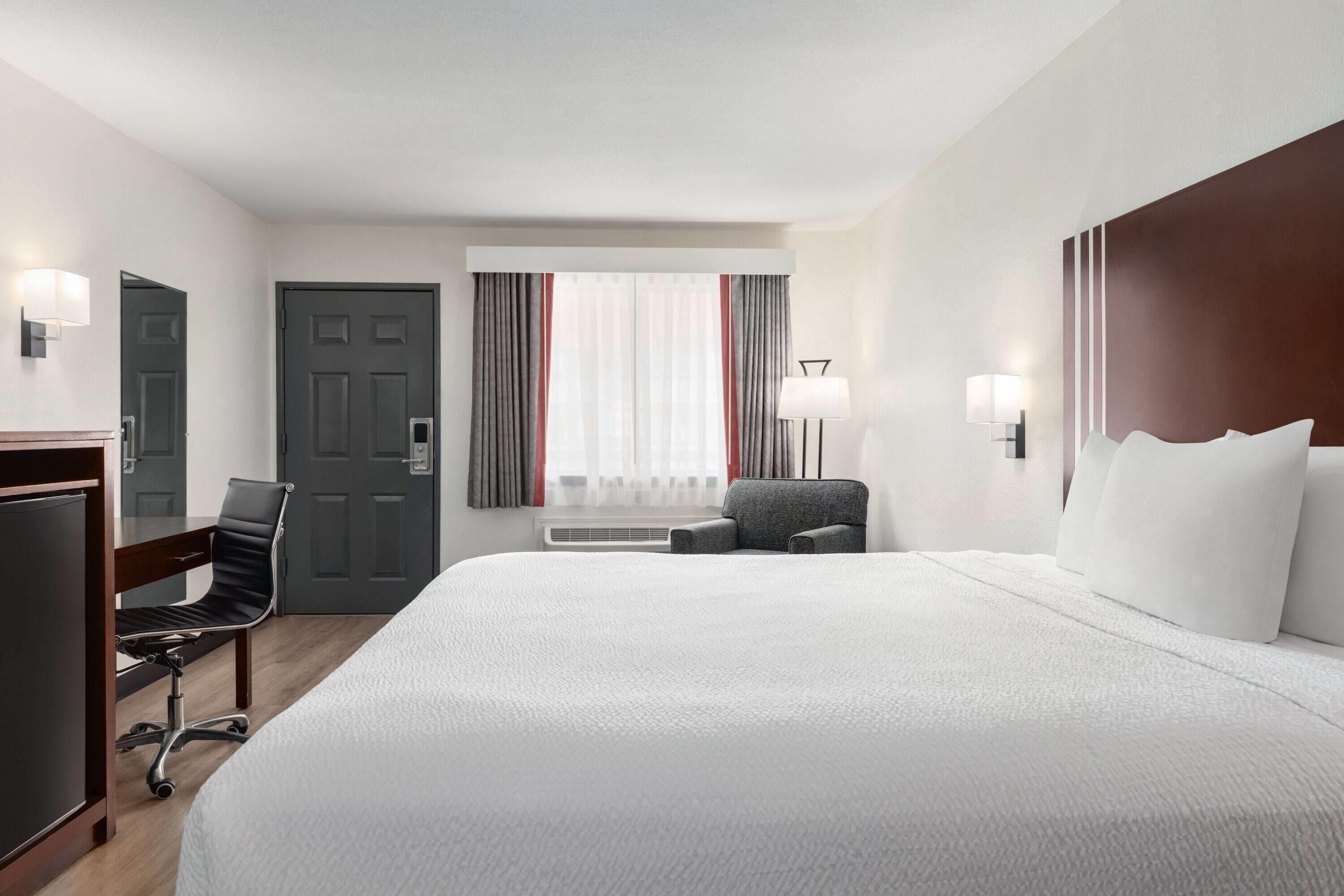 Una habitación de hotel con una cama grande, un escritorio, una silla, una lámpara y una puerta.