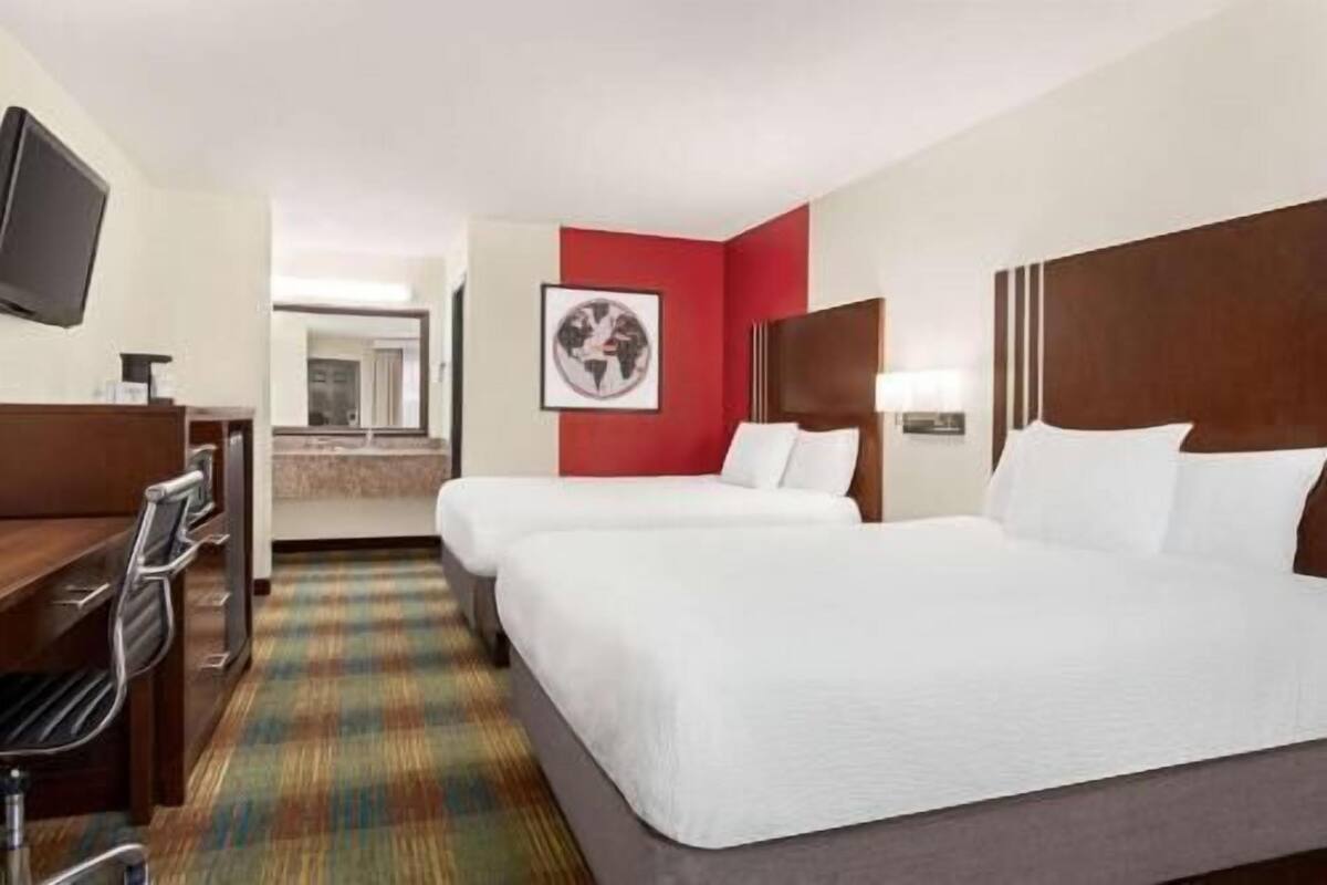 Une chambre d’hôtel avec deux lits, un bureau, une télévision et une salle de bain visible au fond.