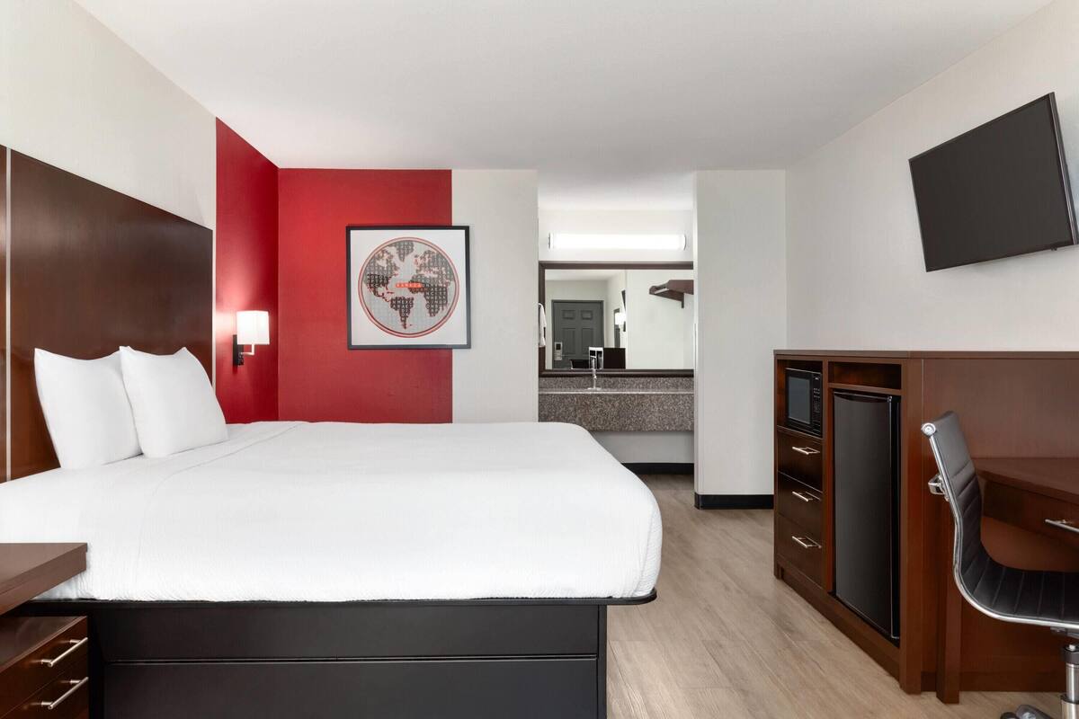 Une chambre d’hôtel équipée d’un lit, d’un bureau, d’une chaise, d’une télévision, d’un four à micro-ondes et d’une petite kitchenette.