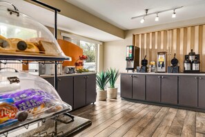 A modern kitchen with a wooden countertop, a coffee station, and a food display. -  Ramada by Wyndham San Antonio Near SeaWorld/Lackland AFB (San Antonio)
