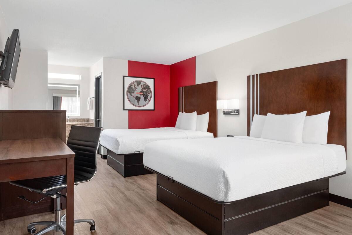 Une chambre d’hôtel avec deux lits, un bureau, une chaise, une télévision et une carte du monde accrochée au mur.