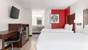 Ein Hotelzimmer mit Schreibtisch, zwei Betten, einem Fernseher und einer roten Akzentwand sowie einer gerahmten Weltkarte.