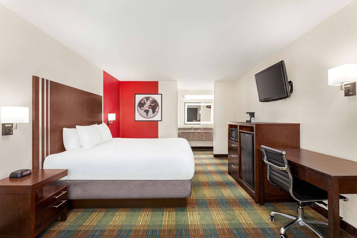 Une chambre d’hôtel avec un lit, un bureau, une chaise, une télévision et un mur d’accent de couleur rouge.