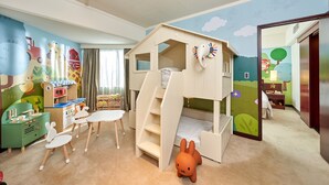 Une chambre d’enfant avec des lits superposés, une cuisine miniature et un ensemble de trains jouets.