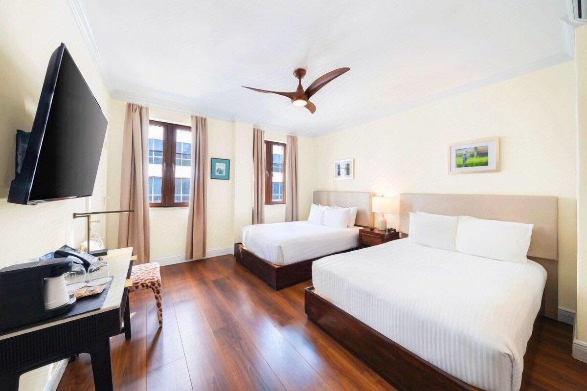 A hotel room with two beds, a flat-screen TV, a desk, and a ceiling fan.