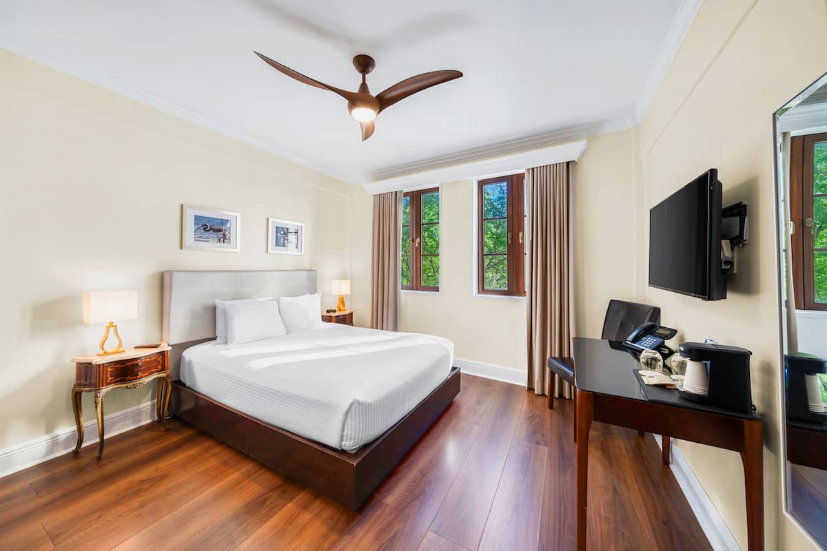 A hotel room with a large bed, a desk with a coffee maker, a television, and a ceiling fan.