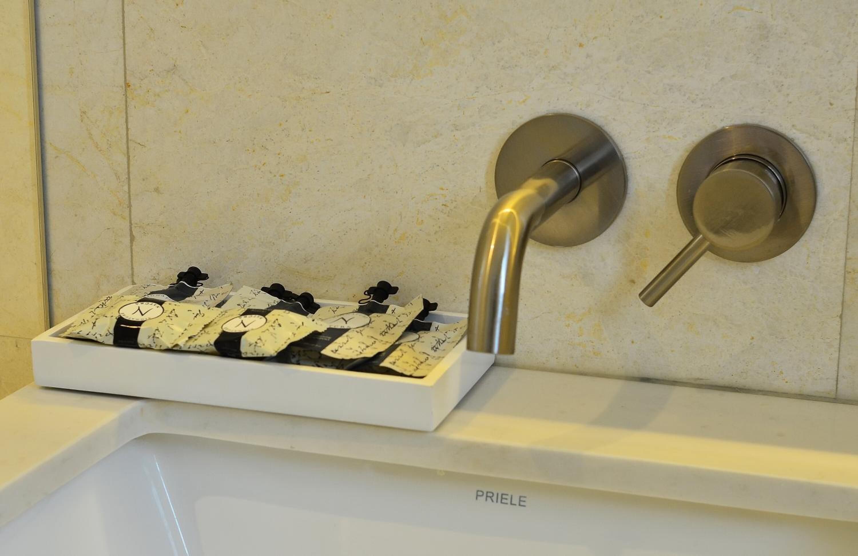 Un baño con un lavamanos blanco, una bandeja blanca que contiene relojes blanco y negro, y un grifo empotrado en la pared.