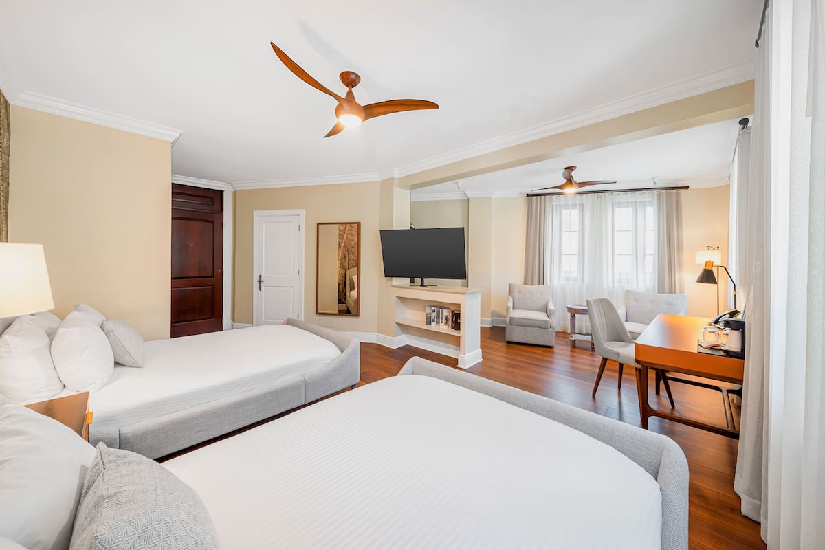 A hotel room with two beds, a TV, a desk with a lamp, and a ceiling fan.