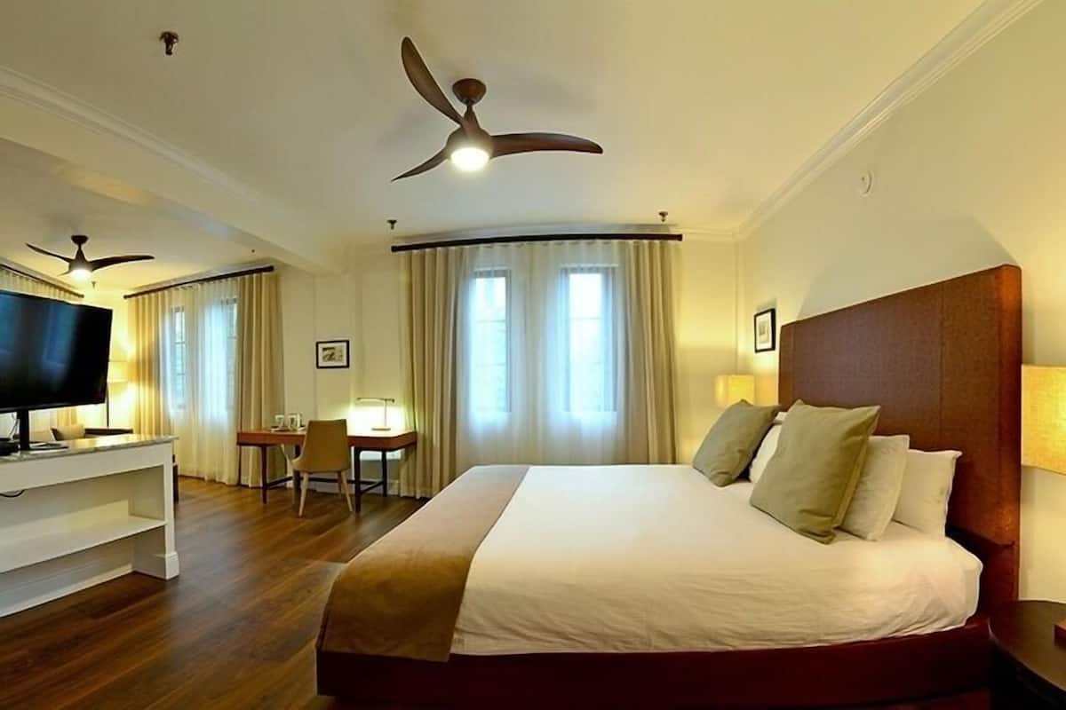 A hotel room with a large bed, a desk, a TV, and a ceiling fan.