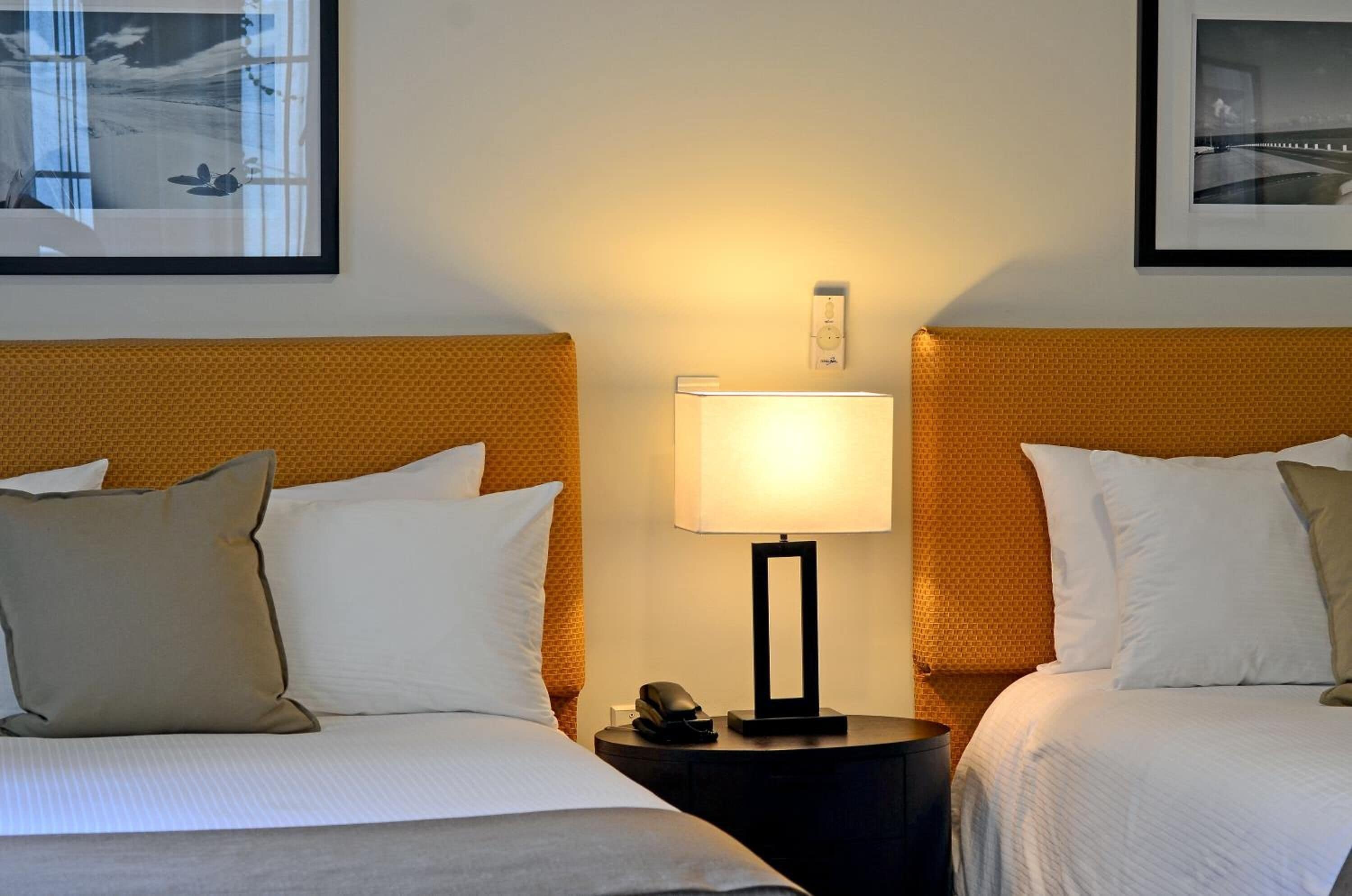 A hotel room with two beds, a nightstand with a lamp, and framed pictures on the wall.