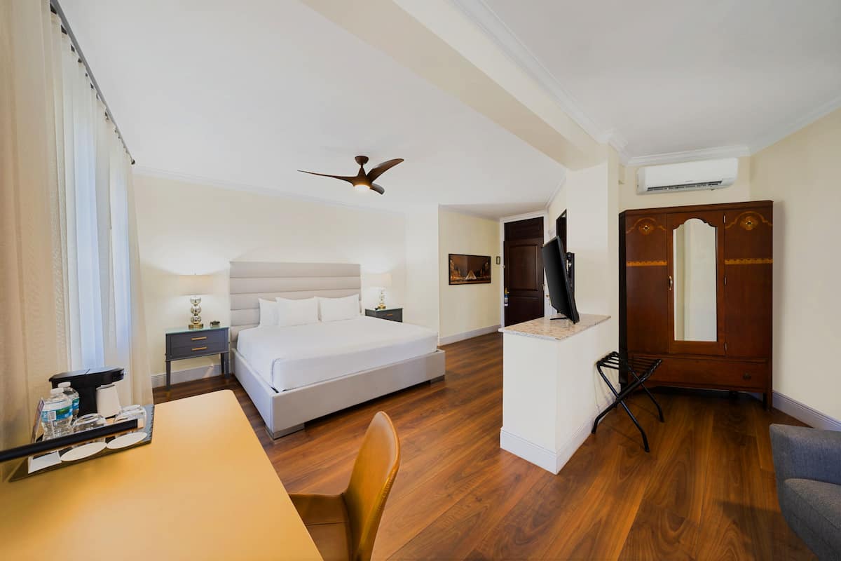 A hotel room with a bed, a desk, a chair, a ceiling fan, and a wardrobe.