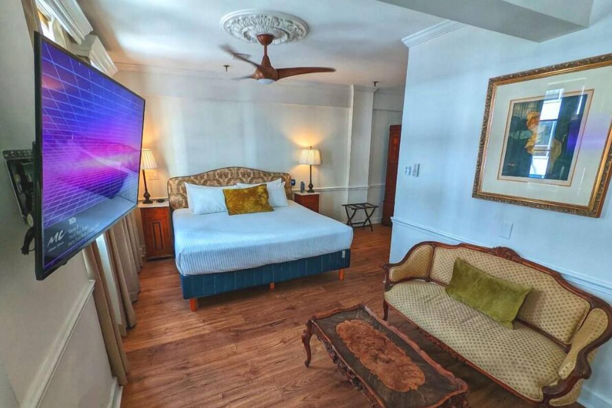 A bedroom with a bed, a TV, a ceiling fan, a sofa, and a small table.
