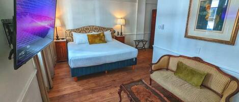 A bedroom with a bed, a TV, a ceiling fan, a sofa, and a small table.