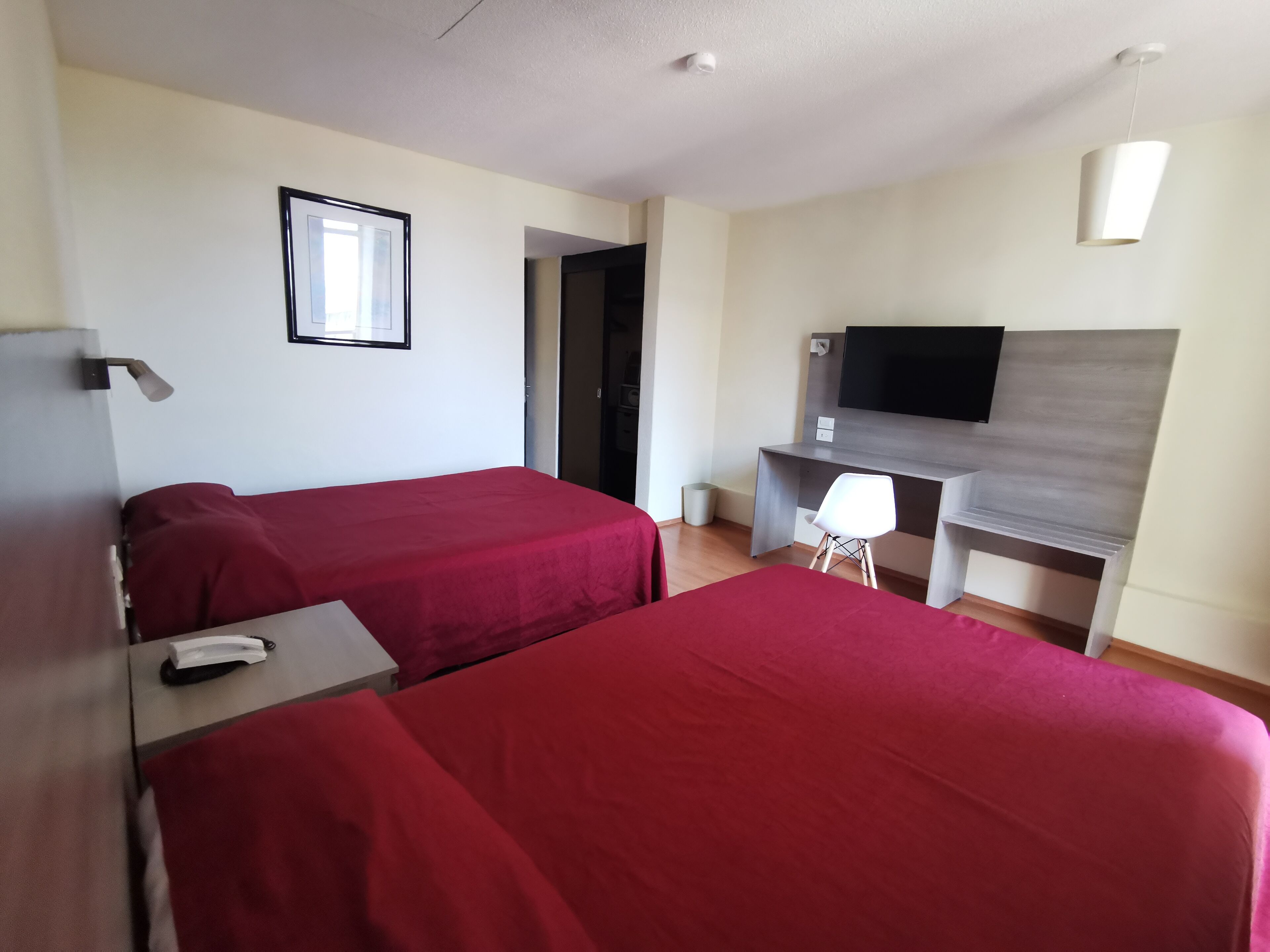 A hotel room with two beds, a desk, a chair, a television, and a framed picture on the wall.