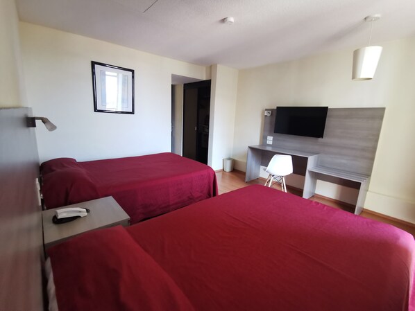 Une chambre d’hôtel avec deux lits, un bureau, une chaise, une télévision et un tableau encadré au mur.