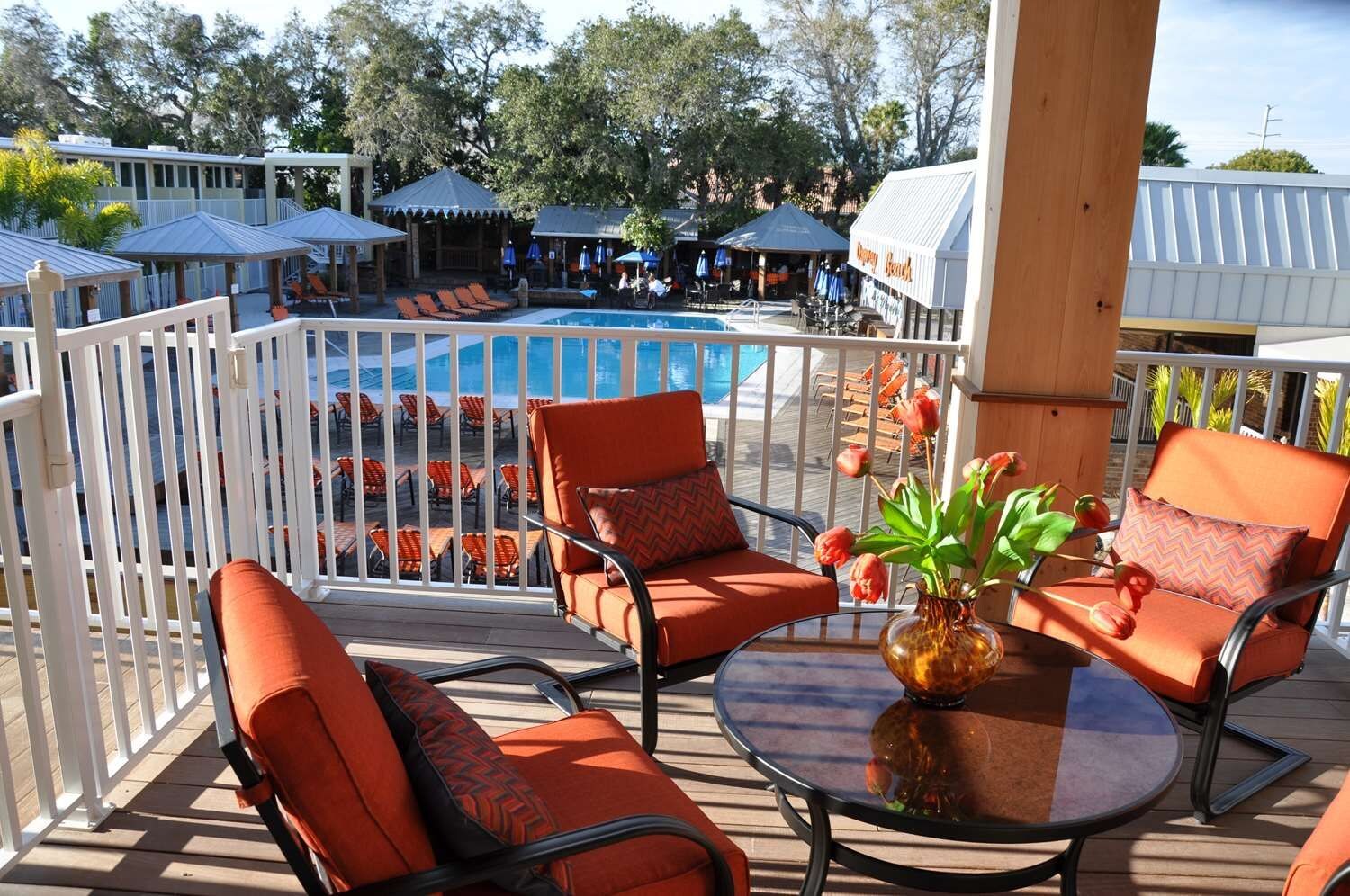 Terraza con sillas anaranjadas y una mesa, con vista a un área de piscina con sombrillas y sillones de descanso.