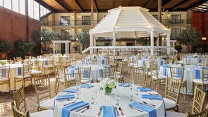 A banquet hall with round tables, gold chairs, and a central white gazebo.