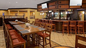A restaurant with multiple dining tables and chairs, a bar area with a counter and stools, and a television mounted on the wall.