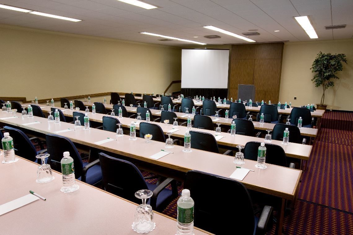 A conference room with multiple tables, chairs, water bottles, and a projector screen.