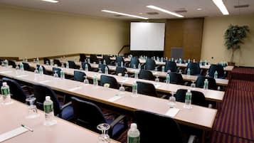 A conference room with multiple tables, chairs, water bottles, and a projector screen.