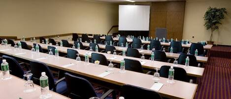 A conference room with multiple tables, chairs, water bottles, and a projector screen.