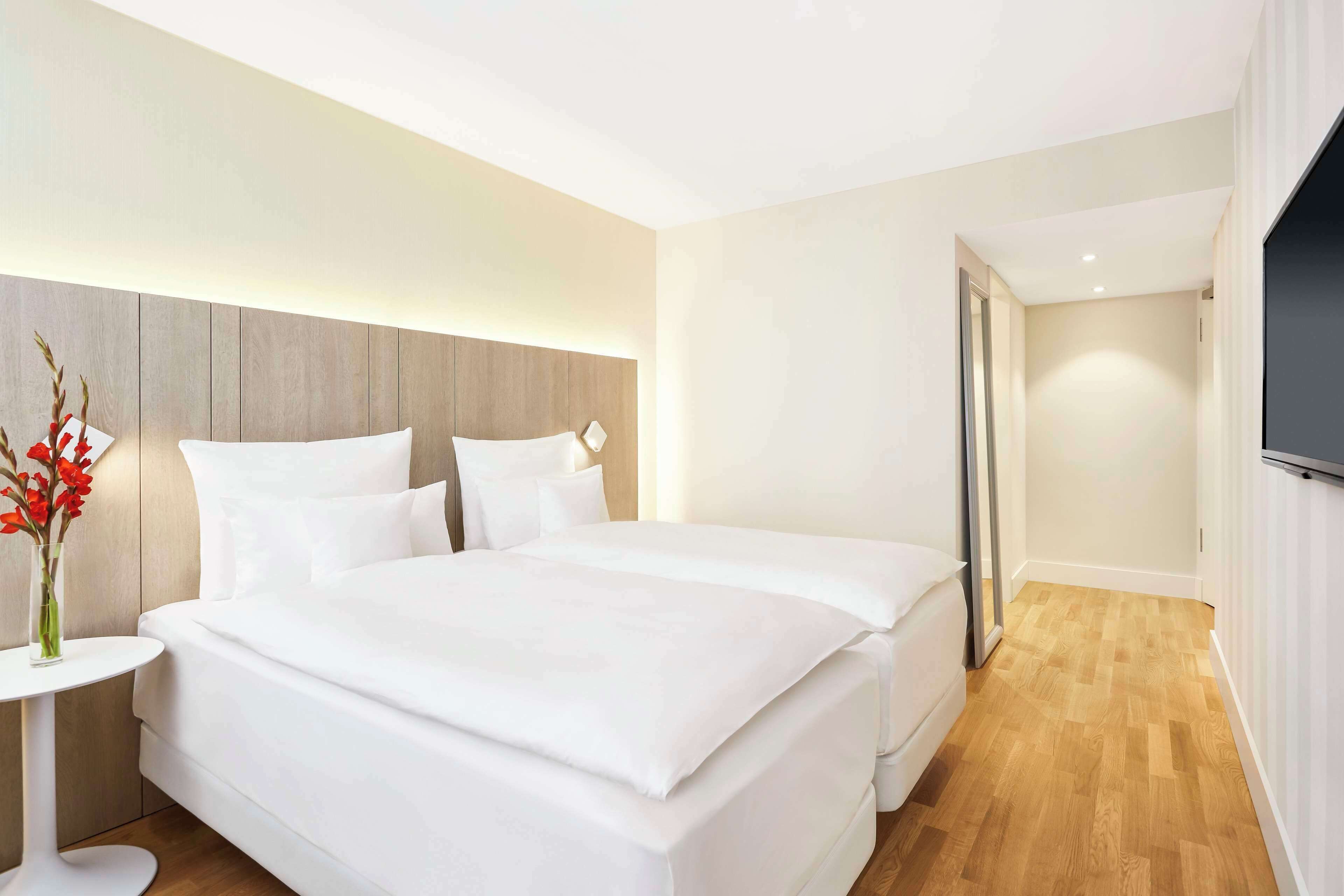 Een hotelkamer met een groot bed, een nachtkastje met een bloevas en een flatscreen televisie aan de muur.