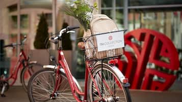 Un vélo avec un panier contenant un bouquet de fleurs et un sac beige, garé devant un immeuble sur lequel on peut lire l’inscription « NH COLLECTION HOTELS ».