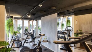 A gym with exercise equipment, large windows, and indoor plants. - NH Collection Hamburg City (Hamburg)