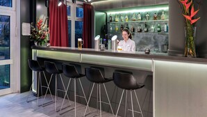 A bar area with a bartender, bar stools, a wine and liquor display, and a large window with curtains. - NH Collection Hamburg City (Hamburg)