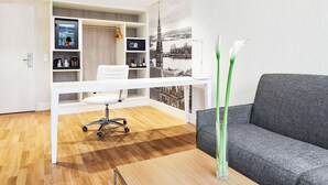 A modern office space with a white desk, grey sofa, and a large wall mural. - NH Collection Hamburg City (Hamburg)