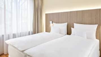 A hotel room with two beds, a wooden headboard, and a window with sheer curtains.