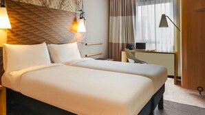 A hotel room with a large bed, two bedside tables, a desk with a chair, a lamp, and a window with curtains. - ibis Quimper (Quimper)