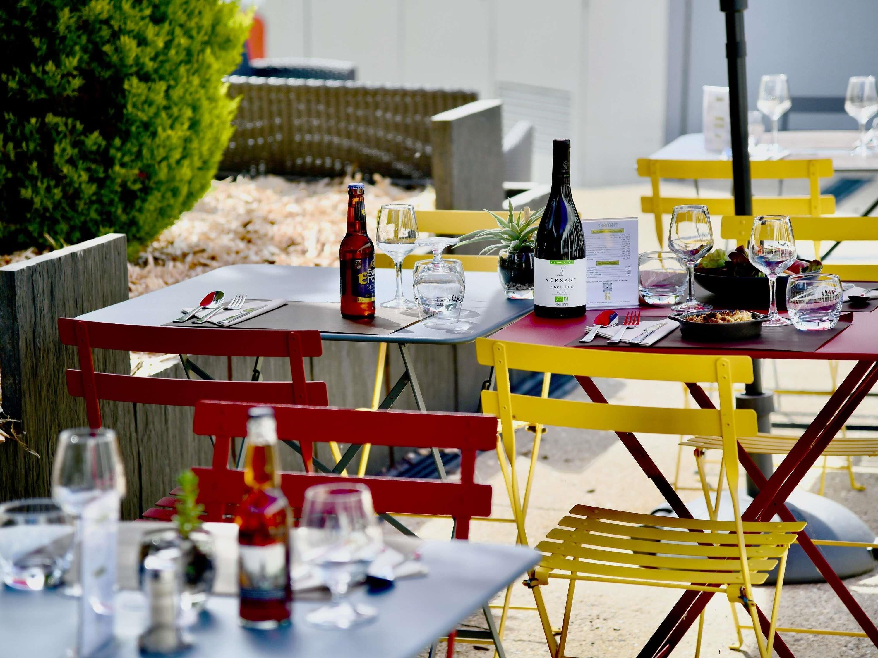 Outdoor dining tables with chairs, wine bottles, glasses, and menus.