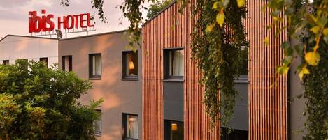 Un moderno edificio de hotel con un letrero que dice 'ibis HOTEL' y una fachada con listones verticales de madera.
