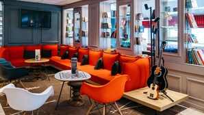 A modern lounge area with orange seating, a small bar, and a guitar. - ibis Quimper (Quimper)
