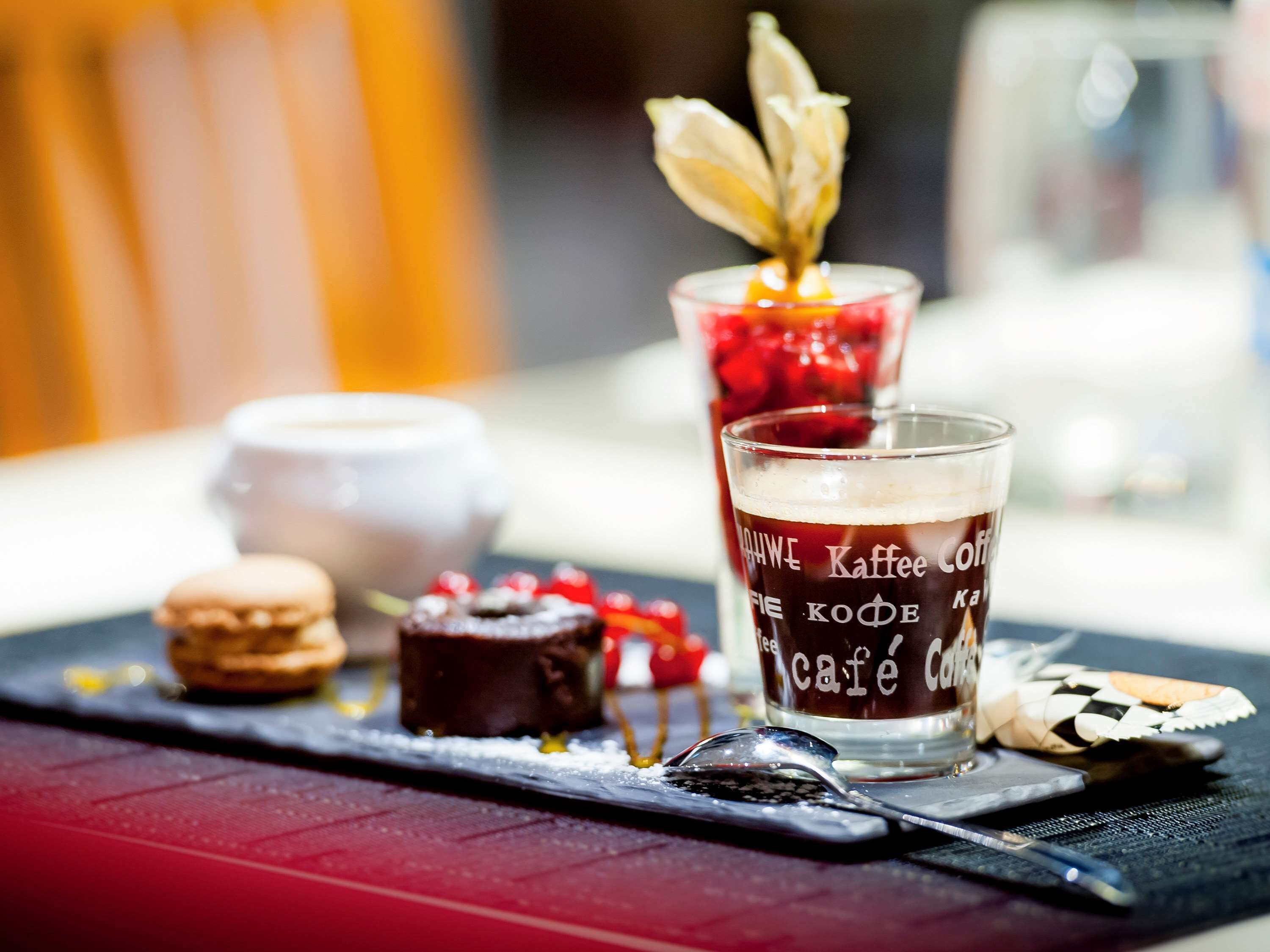 A dessert platter with macarons, a chocolate dessert, and a glass of coffee with a decorative flower on top.