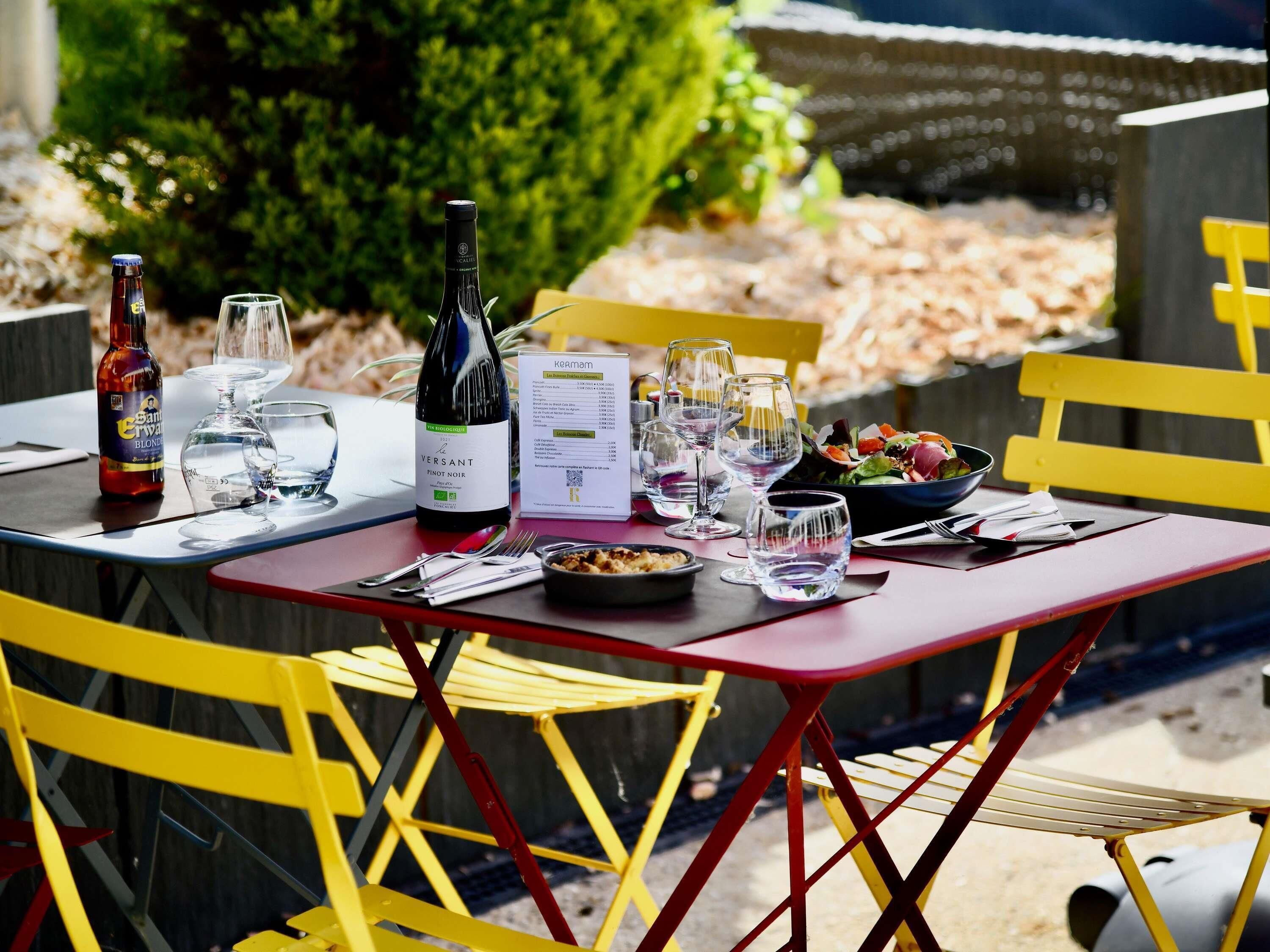 An outdoor dining table with a menu, wine bottle, and glasses.