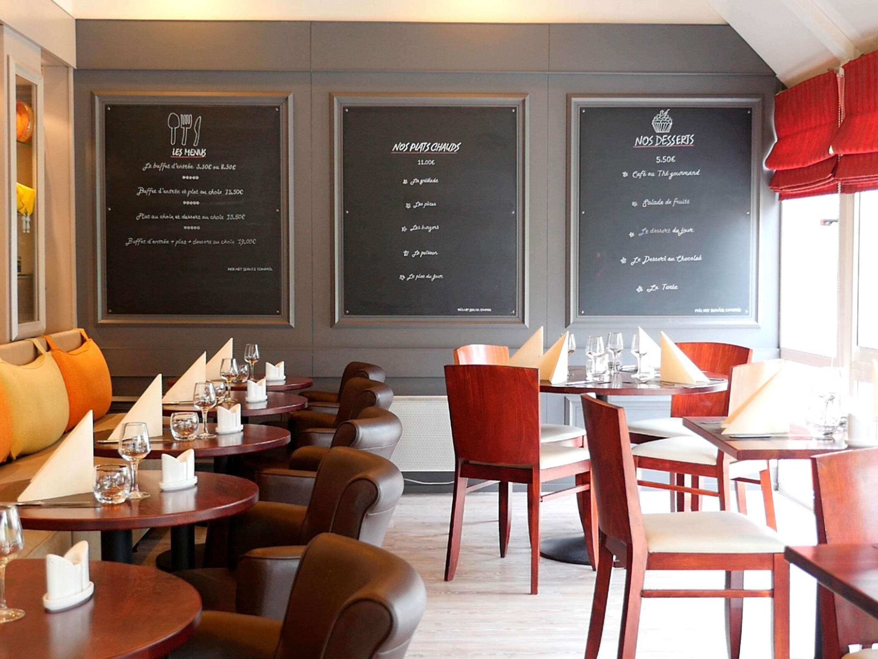 A restaurant interior with round tables, leather chairs, and blackboards displaying menus.