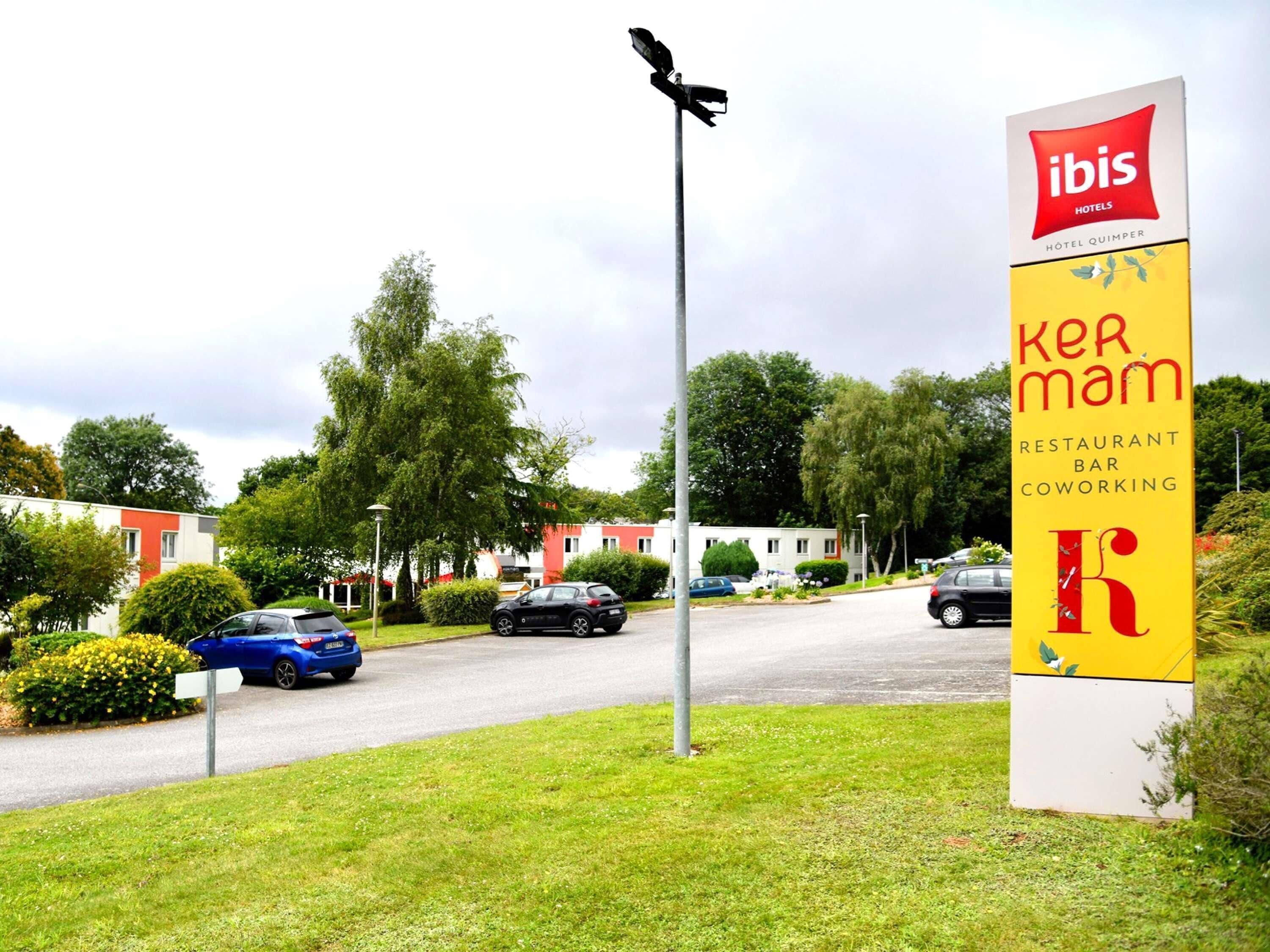Señalización de 'ibis Hotels' y 'ker mam restaurant bar coworking', con una carretera y coches aparcados al fondo.