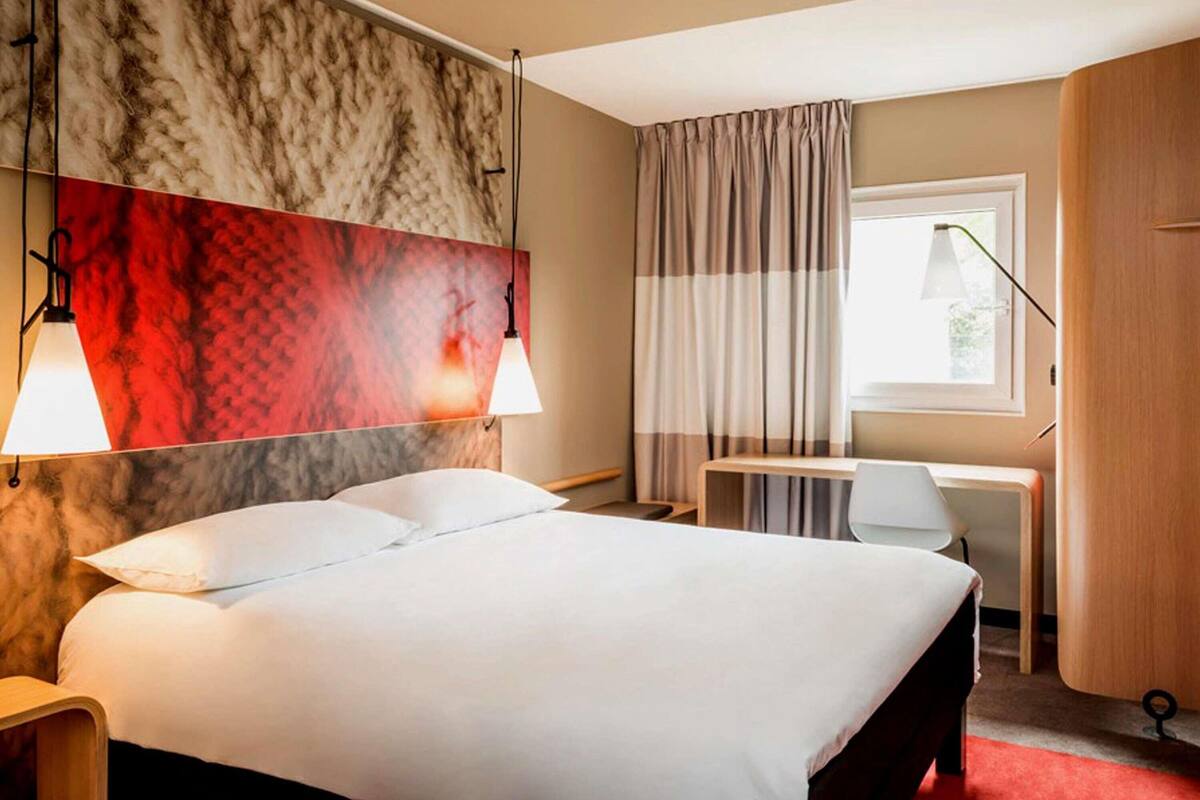 A hotel room with a bed, a desk, a chair, and a wardrobe.