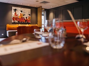 A restaurant setting with a table set for dining, a large abstract painting on the wall, and a view of the outside through a window. - ibis Quimper (Quimper)